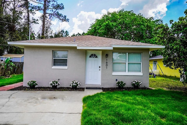 bungalow-style house featuring roof with shingles, a front yard, fence, and stucco siding