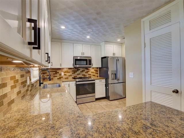 kitchen featuring stainless steel appliances, tasteful backsplash, white cabinetry, a sink, and light stone countertops