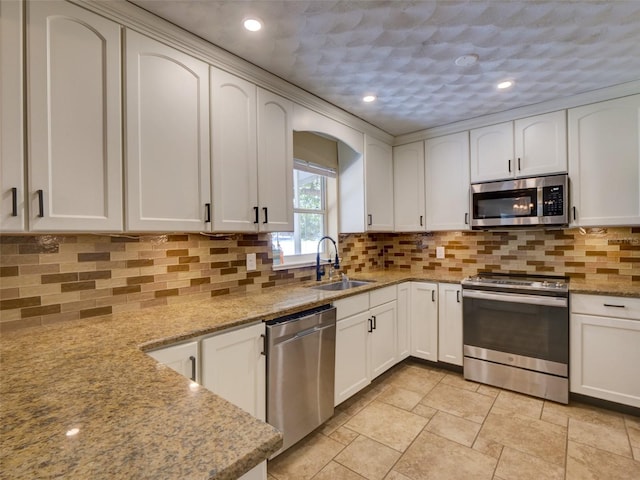 kitchen with stainless steel appliances, a sink, white cabinetry, light stone countertops, and tasteful backsplash