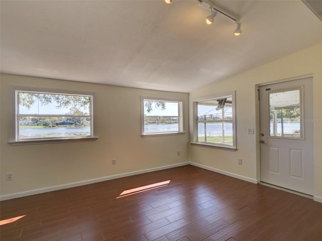 interior space with track lighting, a water view, baseboards, and wood finished floors