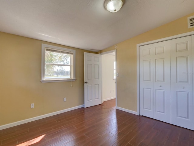 unfurnished bedroom featuring dark wood-style floors, a closet, and baseboards