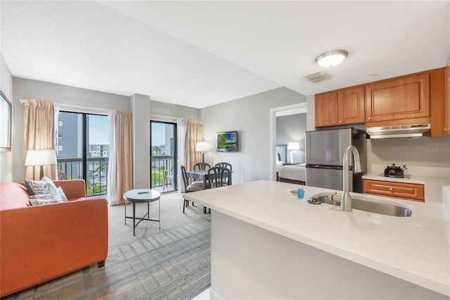 kitchen featuring under cabinet range hood, open floor plan, freestanding refrigerator, and a sink