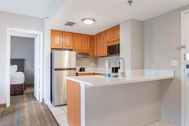 kitchen featuring black microwave, under cabinet range hood, a peninsula, freestanding refrigerator, and a sink