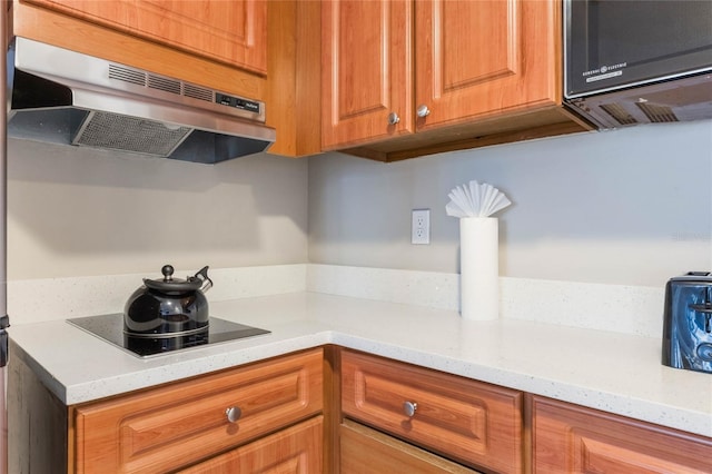 kitchen featuring black appliances, light stone counters, brown cabinetry, and under cabinet range hood