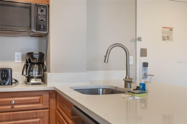 kitchen with a sink, light stone counters, dishwasher, and brown cabinetry