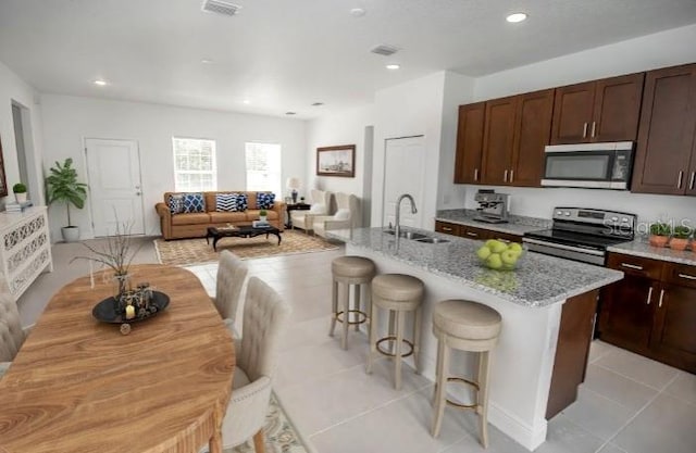 kitchen featuring a kitchen bar, stainless steel appliances, light stone countertops, a sink, and a kitchen island with sink