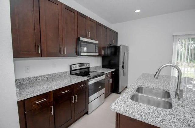 kitchen featuring recessed lighting, a sink, light stone counters, dark brown cabinets, and appliances with stainless steel finishes