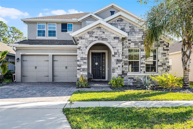 view of front of home with decorative driveway, roof with shingles, stucco siding, an attached garage, and stone siding