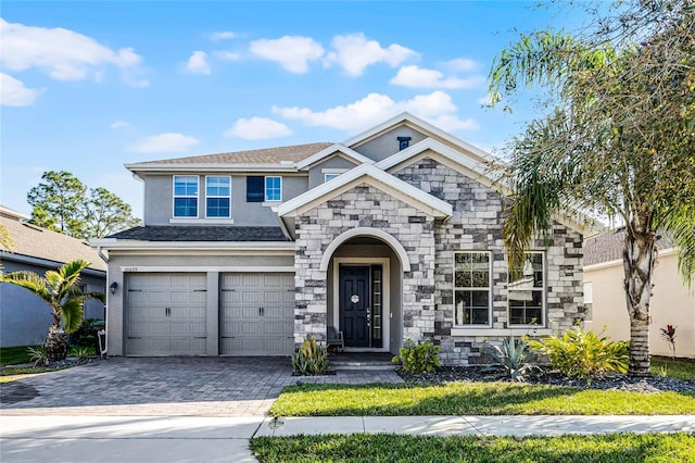 view of front facade featuring a garage, decorative driveway, stone siding, and stucco siding