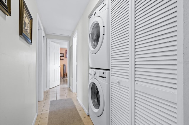 laundry room with light tile patterned floors, laundry area, stacked washer and clothes dryer, and baseboards