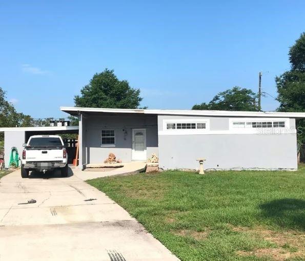 ranch-style home with driveway, a front yard, an attached carport, and stucco siding