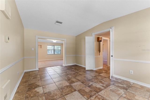 spare room with baseboards, visible vents, a textured ceiling, and lofted ceiling