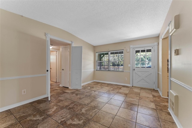 foyer entrance featuring a textured ceiling, baseboards, and vaulted ceiling