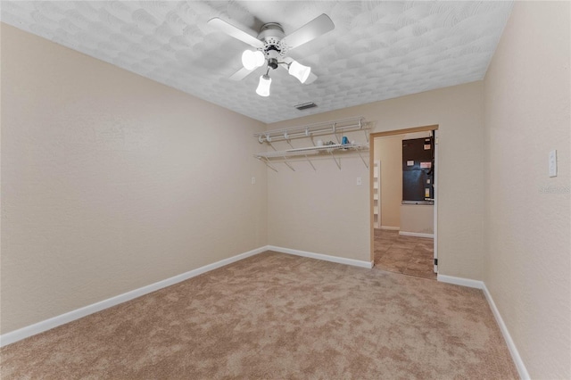 interior space with visible vents, baseboards, light colored carpet, a textured wall, and a ceiling fan