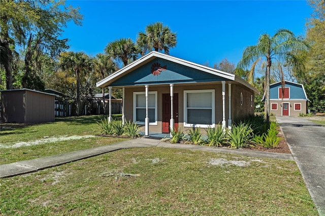 bungalow-style home with stucco siding, a front lawn, a porch, a shed, and an outdoor structure