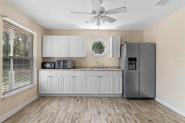 kitchen featuring visible vents, a sink, white cabinetry, stainless steel fridge, and light wood finished floors