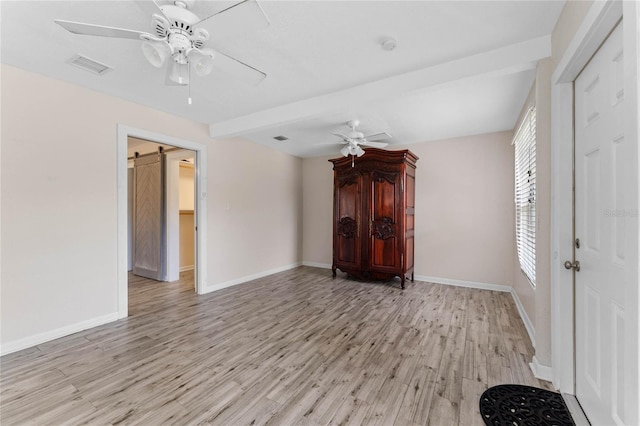 interior space featuring visible vents, baseboards, ceiling fan, a barn door, and light wood-style flooring