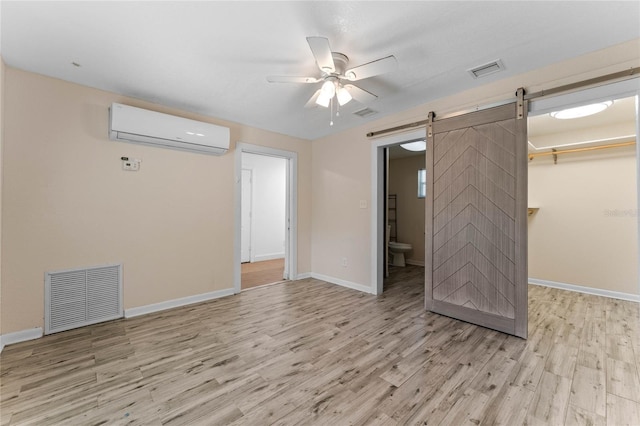 unfurnished bedroom with an AC wall unit, a barn door, visible vents, and light wood-type flooring