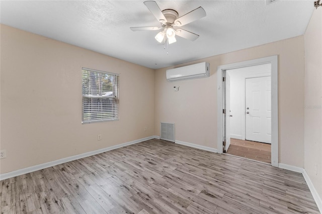 unfurnished room with light wood finished floors, visible vents, baseboards, ceiling fan, and a wall mounted air conditioner