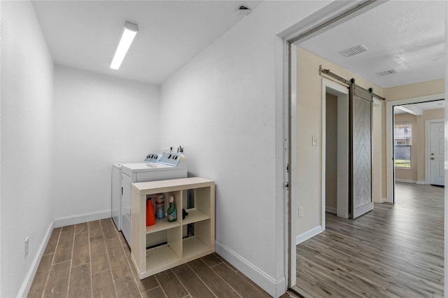 laundry room with visible vents, dark wood-type flooring, a barn door, laundry area, and independent washer and dryer