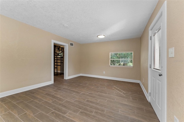 unfurnished room with a textured ceiling, baseboards, visible vents, and wood finish floors