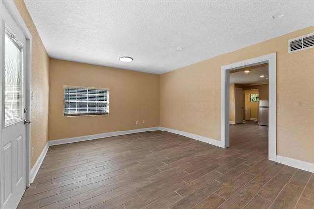 unfurnished room with a wealth of natural light, visible vents, baseboards, and dark wood-style flooring