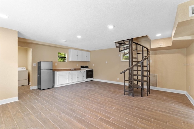 kitchen featuring washer / dryer, white gas stove, freestanding refrigerator, white cabinets, and light wood-type flooring