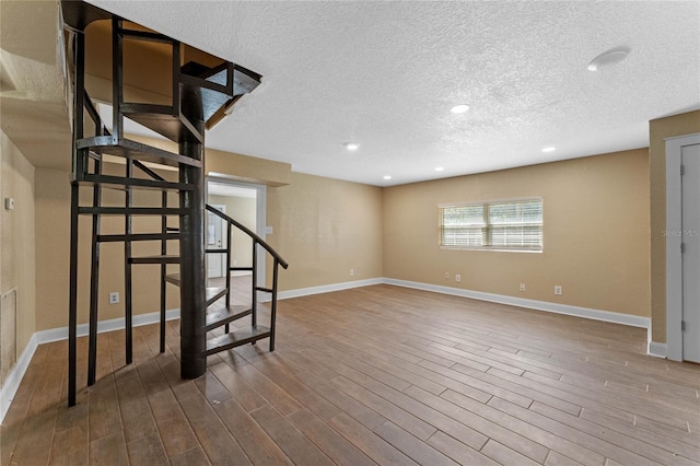 below grade area featuring a textured ceiling, dark wood finished floors, recessed lighting, baseboards, and stairs