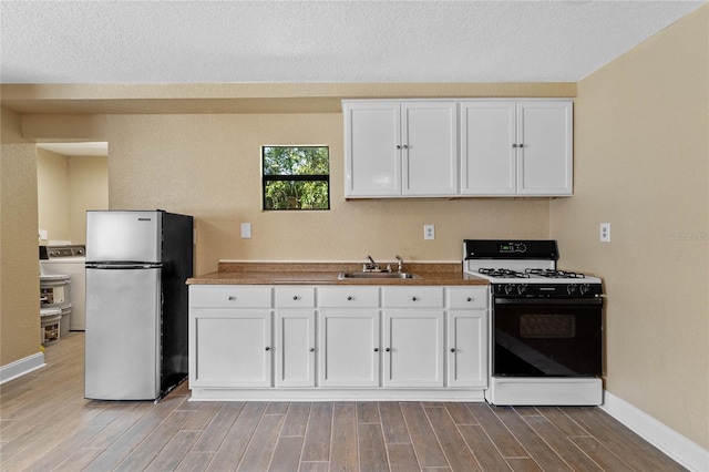 kitchen featuring wood tiled floor, gas range, freestanding refrigerator, white cabinetry, and a sink