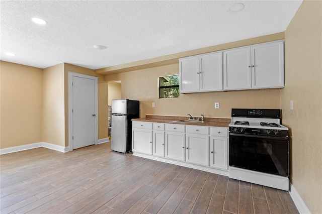 kitchen featuring white cabinetry, wood finished floors, gas range oven, and freestanding refrigerator