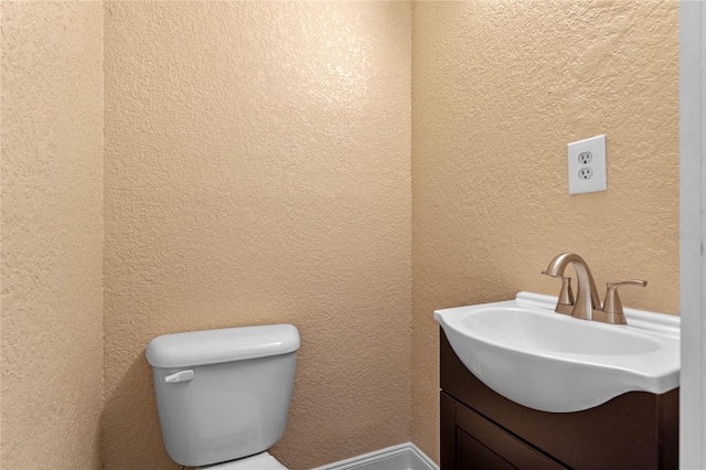 bathroom featuring toilet, vanity, and a textured wall