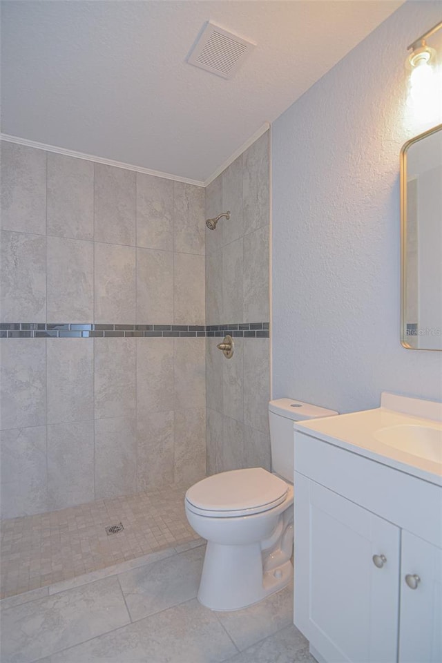 bathroom with tile patterned flooring, toilet, vanity, visible vents, and tiled shower