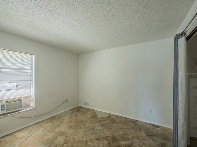 spare room featuring baseboards, a textured ceiling, visible vents, and cooling unit