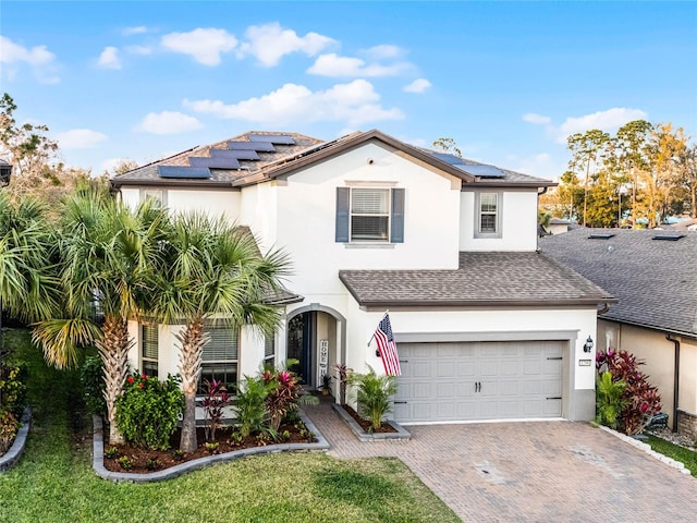 view of front facade featuring a shingled roof, decorative driveway, solar panels, and stucco siding