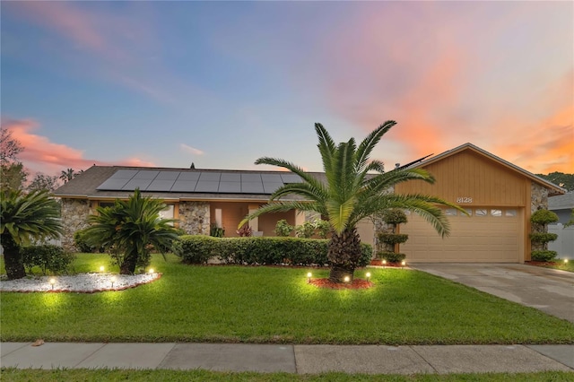 view of front facade featuring a garage, driveway, a front lawn, and solar panels