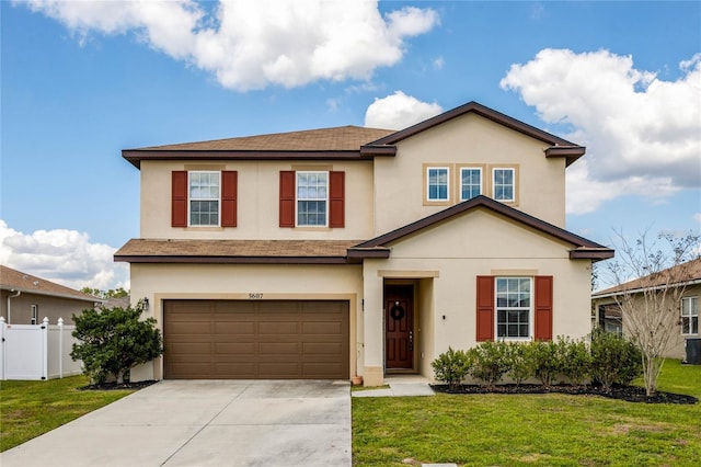 traditional-style house featuring a garage, fence, driveway, stucco siding, and a front yard