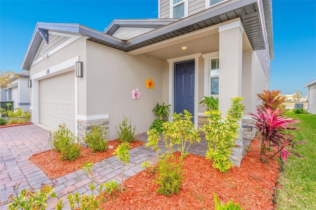 entrance to property with a garage, stone siding, driveway, and stucco siding