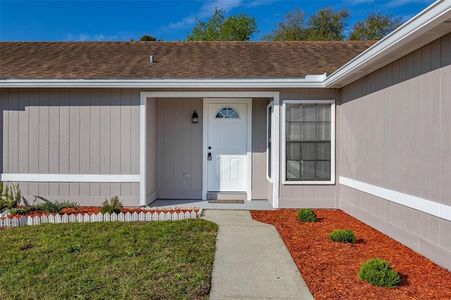 doorway to property featuring a yard and roof with shingles