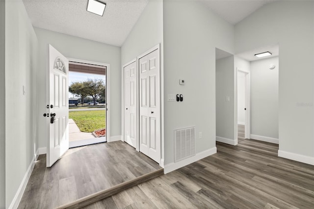 entryway featuring baseboards, visible vents, wood finished floors, vaulted ceiling, and a textured ceiling