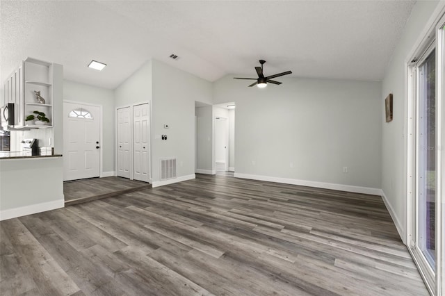 interior space with dark wood-type flooring, a ceiling fan, visible vents, vaulted ceiling, and baseboards