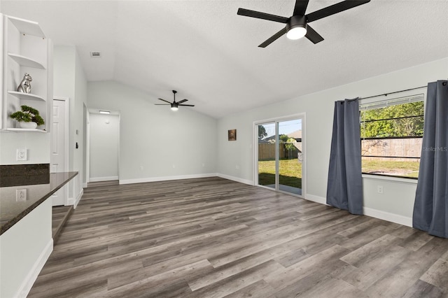 unfurnished living room featuring dark wood-style floors, lofted ceiling, a textured ceiling, and baseboards