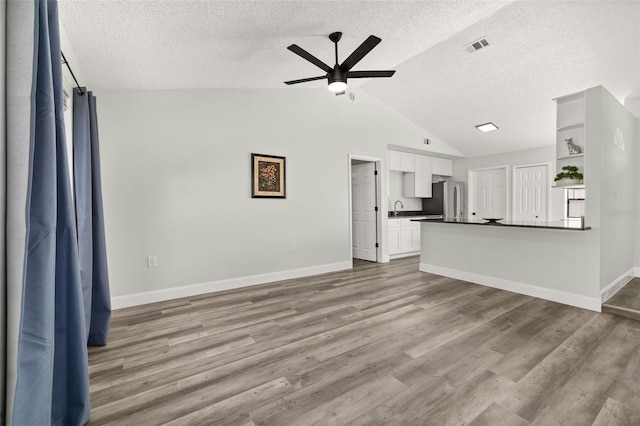 unfurnished living room with lofted ceiling, ceiling fan, wood finished floors, and baseboards