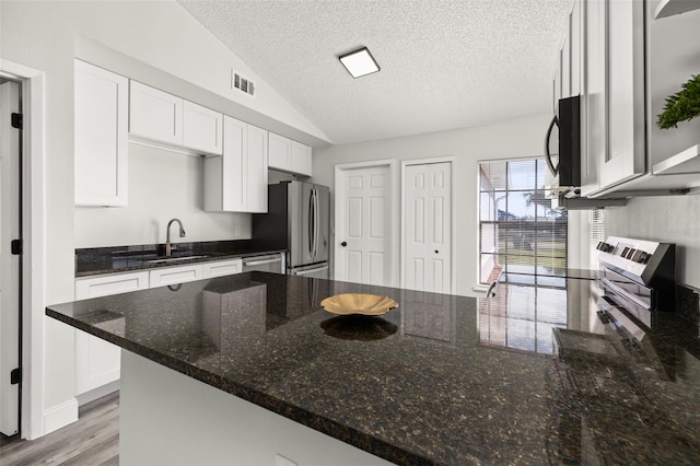 kitchen with visible vents, lofted ceiling, dark stone countertops, stainless steel appliances, and a sink