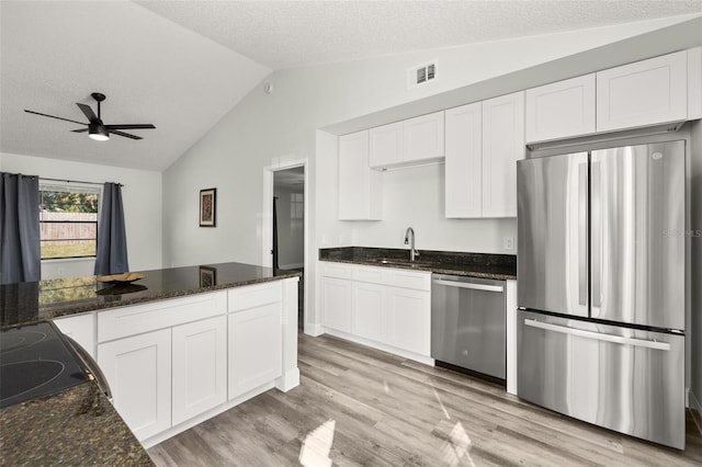 kitchen with white cabinets, dark stone countertops, vaulted ceiling, stainless steel appliances, and light wood-type flooring