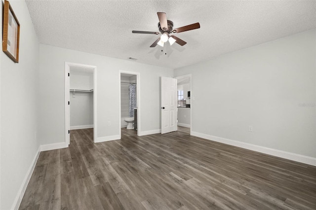 unfurnished bedroom with a textured ceiling, dark wood-type flooring, baseboards, a closet, and a walk in closet