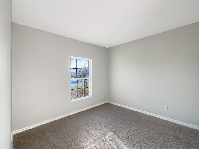 spare room featuring dark carpet and baseboards