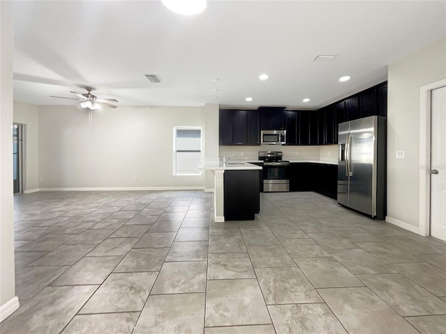 kitchen with open floor plan, stainless steel appliances, dark cabinetry, and light countertops