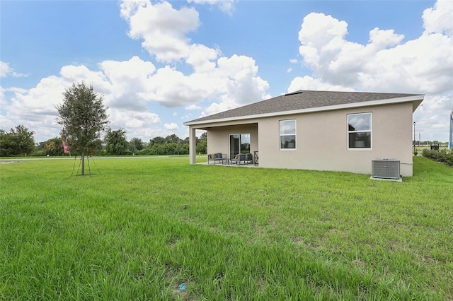 rear view of house featuring a patio, stucco siding, a shingled roof, a lawn, and central AC