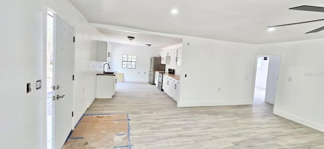 kitchen featuring a ceiling fan, appliances with stainless steel finishes, light wood-style floors, white cabinetry, and a sink