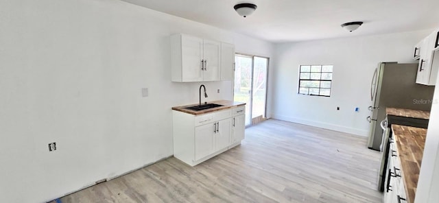 kitchen featuring baseboards, light wood-type flooring, a sink, and white cabinets